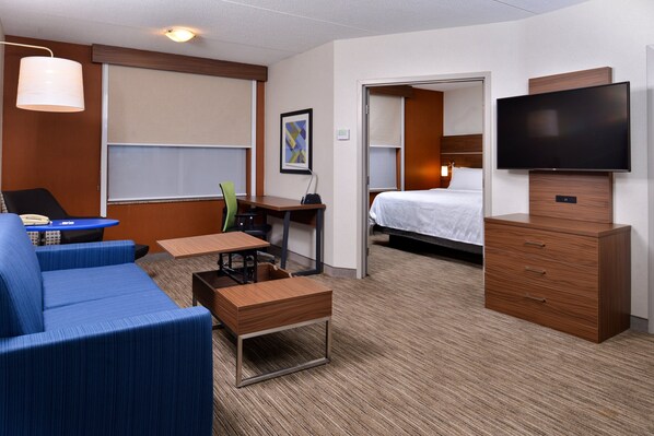 A hotel room with a bed, a desk, a chair, a TV, and a sofa.