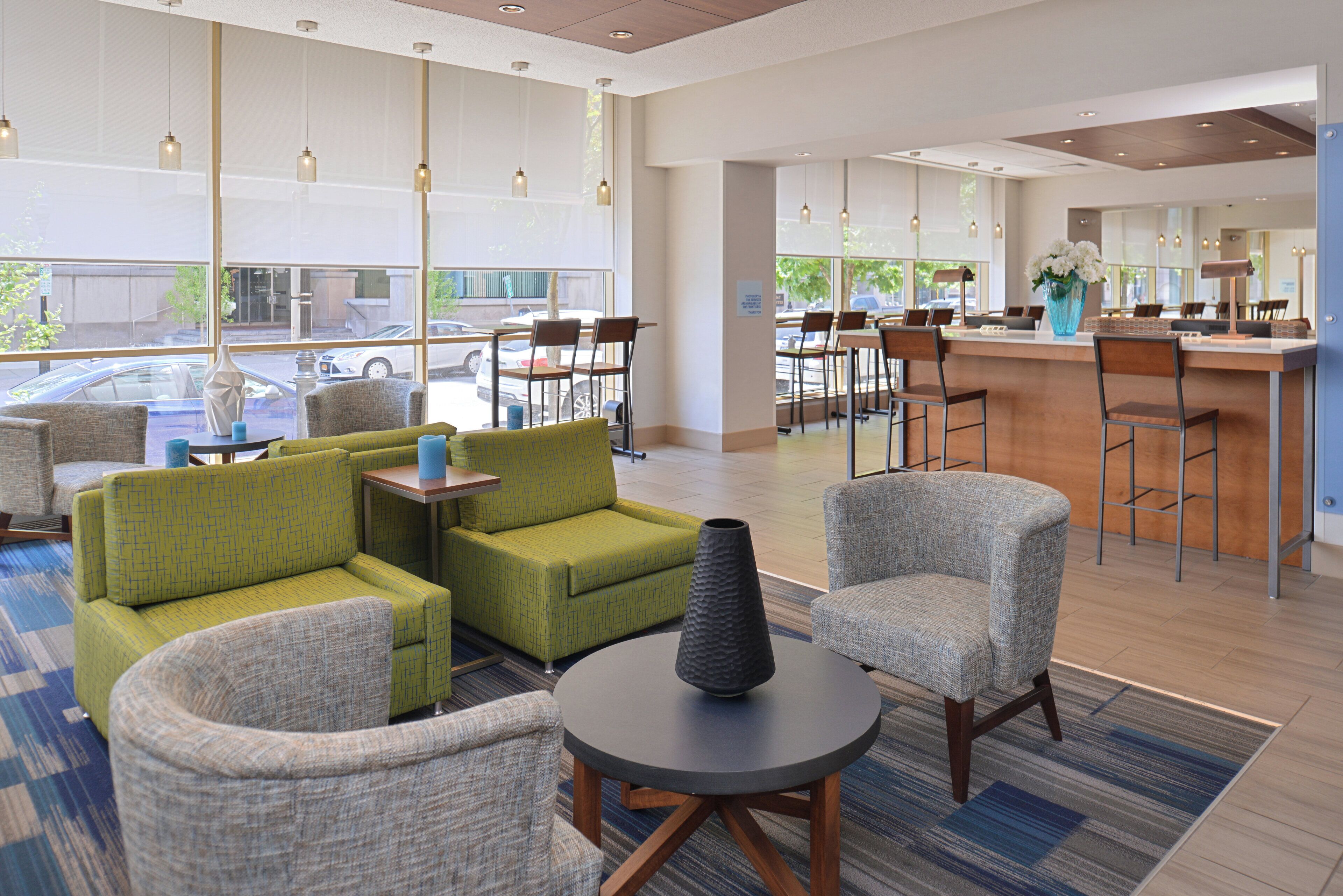 A hotel lobby with seating areas, a reception desk, and large windows overlooking the street.