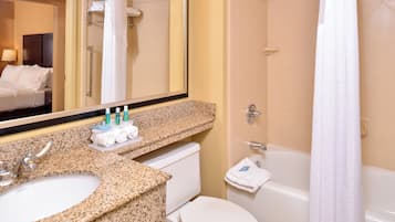 Une salle de bain avec un lavabo sur un plan de travail en granit, des toilettes, une baignoire et un miroir.