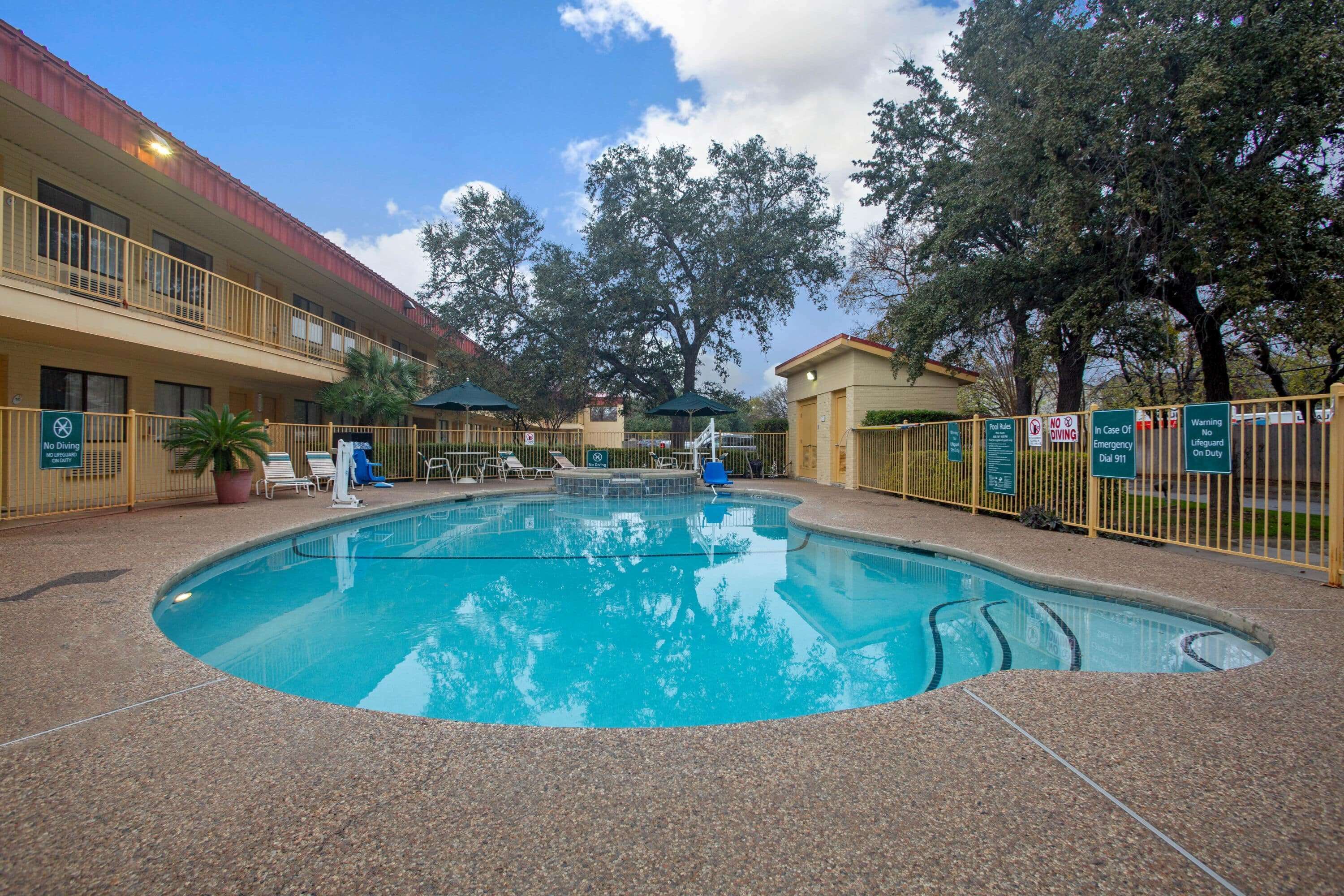 A hotel with a swimming pool, outdoor seating, and a fenced area.