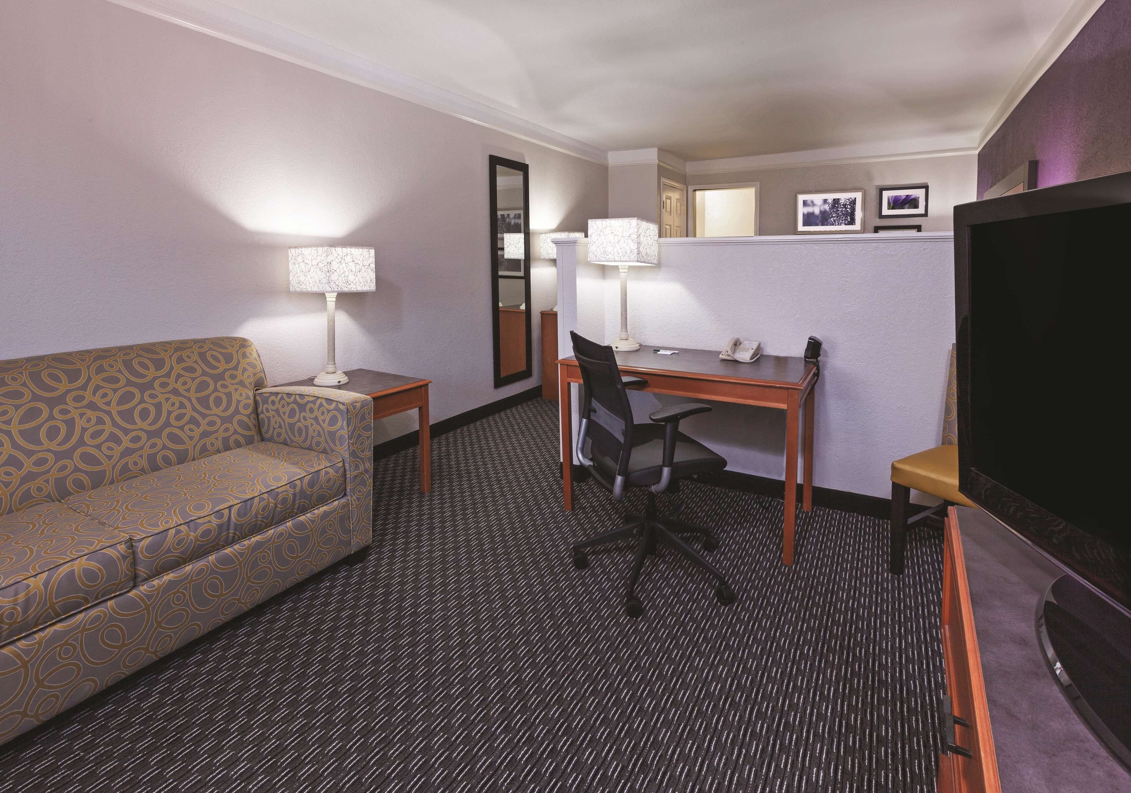 A hotel room with a sofa, a desk, a chair, a TV, and two lamps.