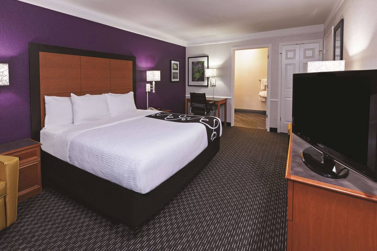 A hotel room with a large bed, a desk, a TV, and a bathroom visible through an open door.