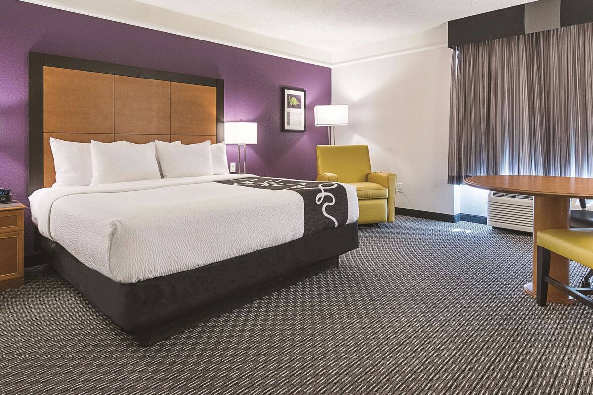A hotel room with a large bed, a chair, a table, and a lamp.