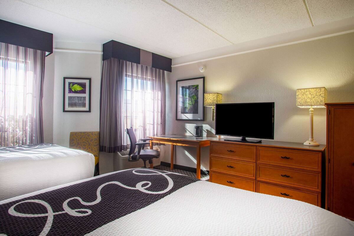 A hotel room with two beds, a desk with a television, a chair, and a dresser.