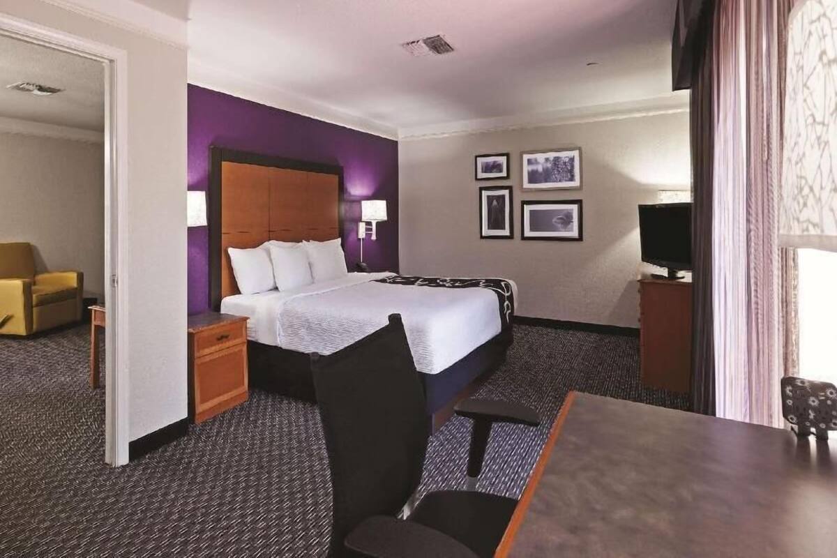 A hotel room with a bed, a desk, a chair, a TV, and a small table.