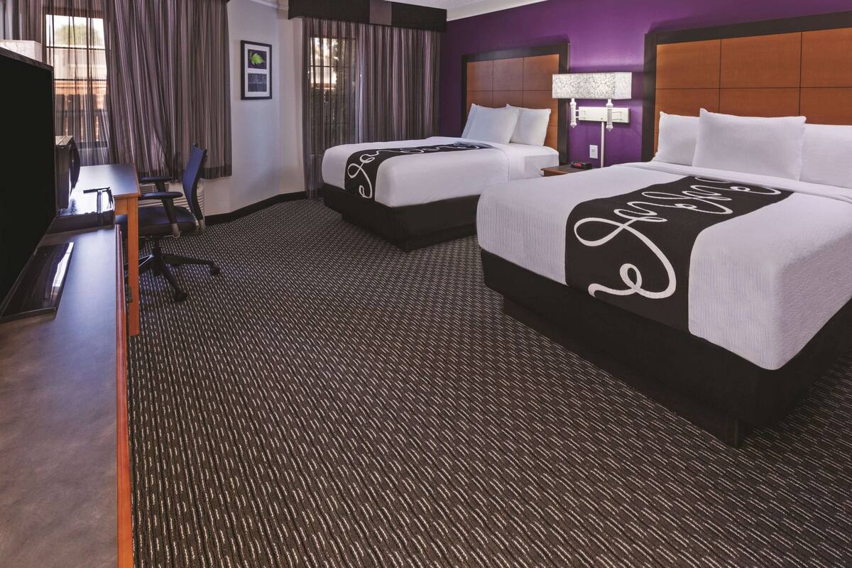 A hotel room with two beds, a desk, a chair, a TV, and a window with curtains.