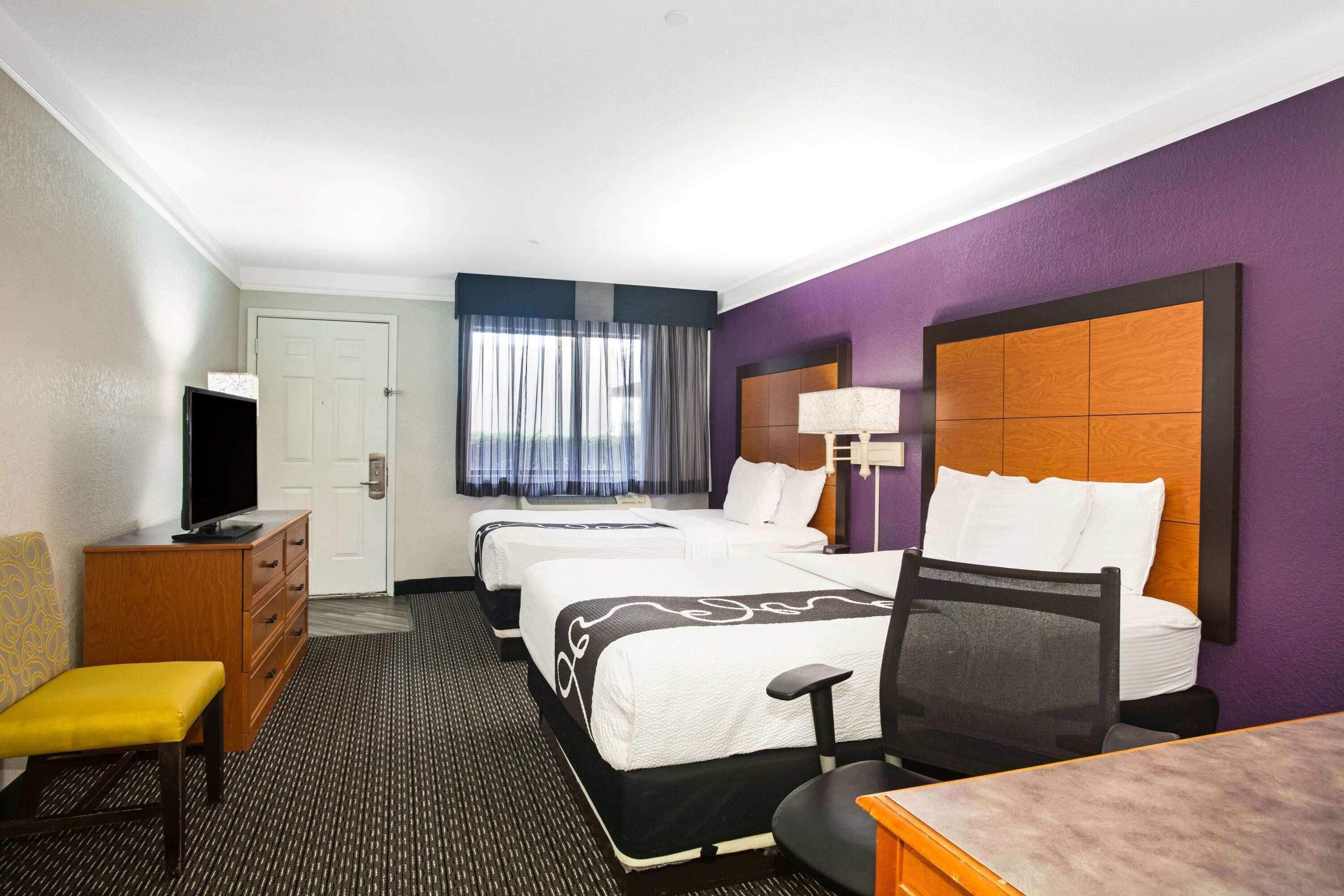 A hotel room with two beds, a desk, a chair, a television, and a window with curtains.