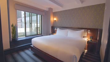 A hotel room with a large bed, a nightstand, a wall-mounted lamp, and a window with blinds.