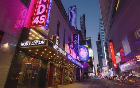 A hotel with a neon sign, a theater marquee, and a tall building in the background.