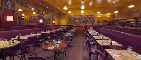 A restaurant with booths and tables, wooden floors, and hanging lights.