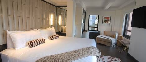Habitación de hotel moderna con una cama grande, un sofá, un televisor y vistas a la ciudad.