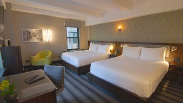 A hotel room with two beds, a desk, a chair, a window, and a wall with a cityscape painting.