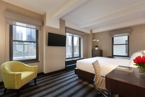 Quarto de hotel com uma cama grande, uma escrivaninha, uma cadeira, uma televisão e uma janela com vista para a cidade.