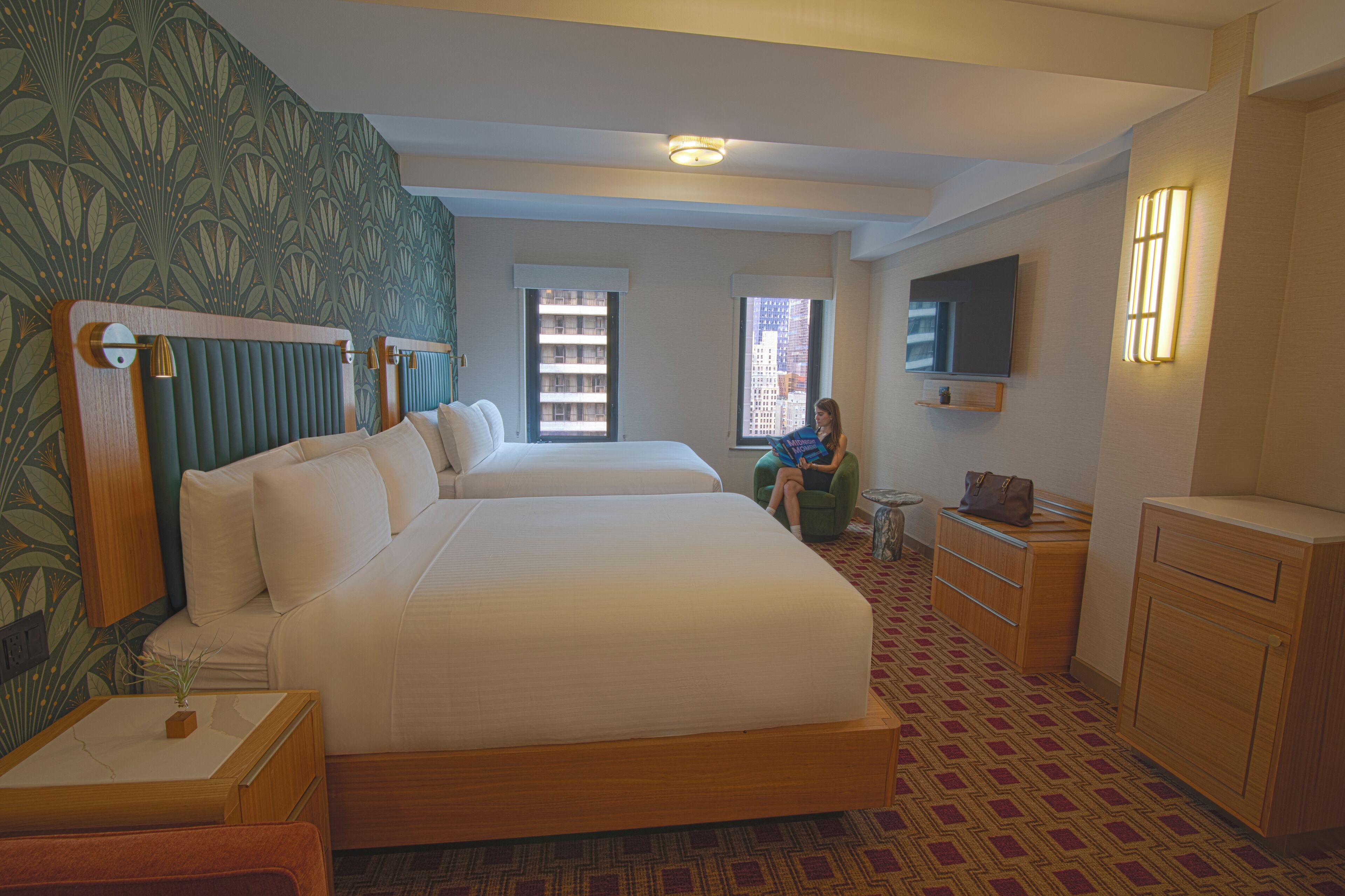 Habitación de hotel con dos camas, televisión, escritorio y ventana con vistas a la ciudad.