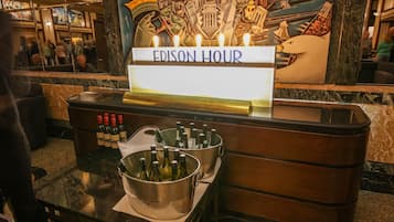 Zona de bar con un cartel que dice "EDISON HOUR" y dos cubos grandes llenos de botellas, probablemente para servir bebidas.