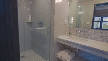 A modern bathroom with a glass-enclosed shower, a vanity with a marble countertop, and a view of buildings through a window.