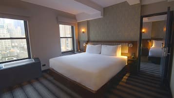 A hotel room with a large bed, a window with a city view, a built-in heater, and a mirror in the corner.