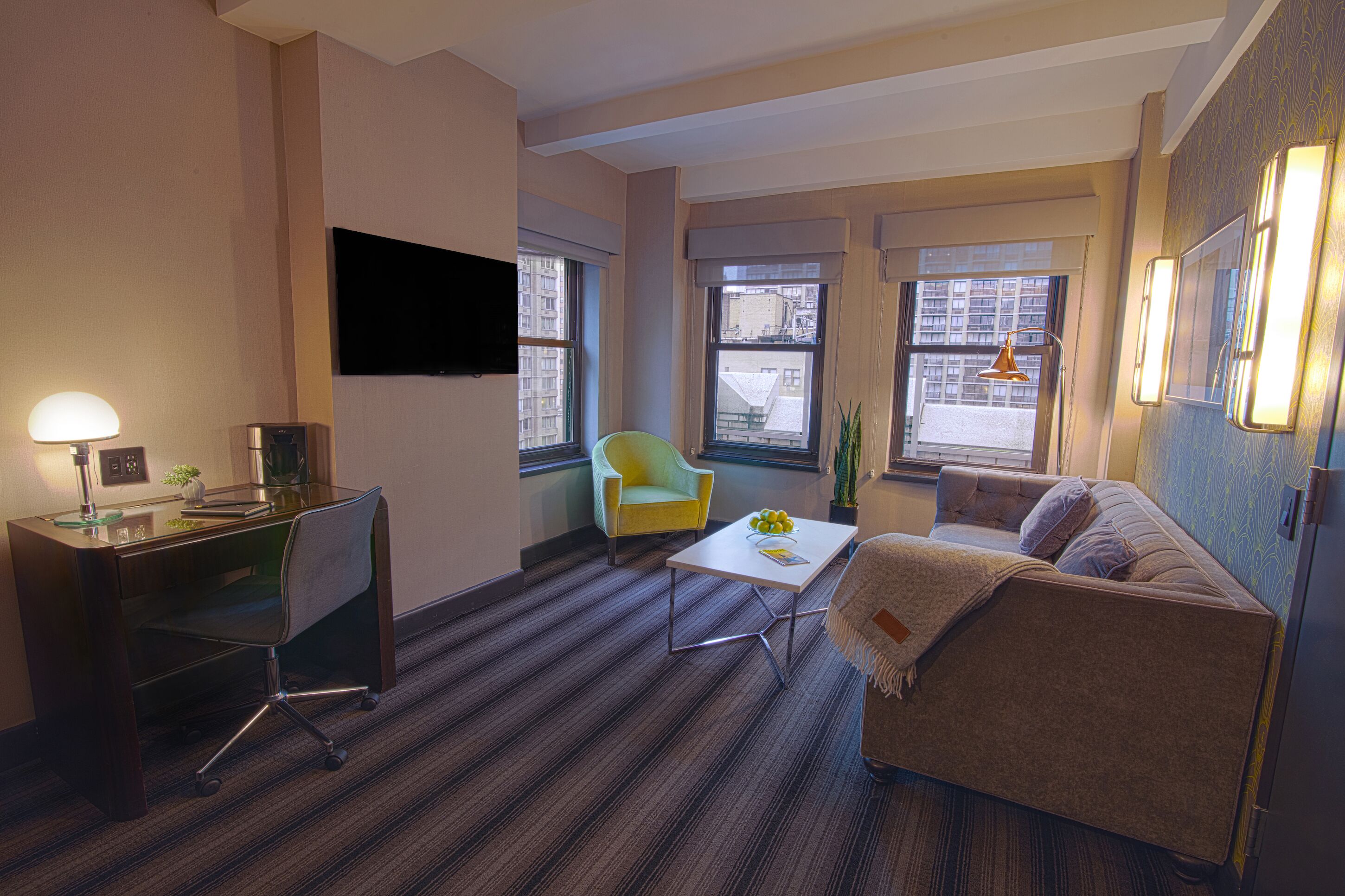 A modern hotel room with a desk, a yellow armchair, a white coffee table, and a sofa.