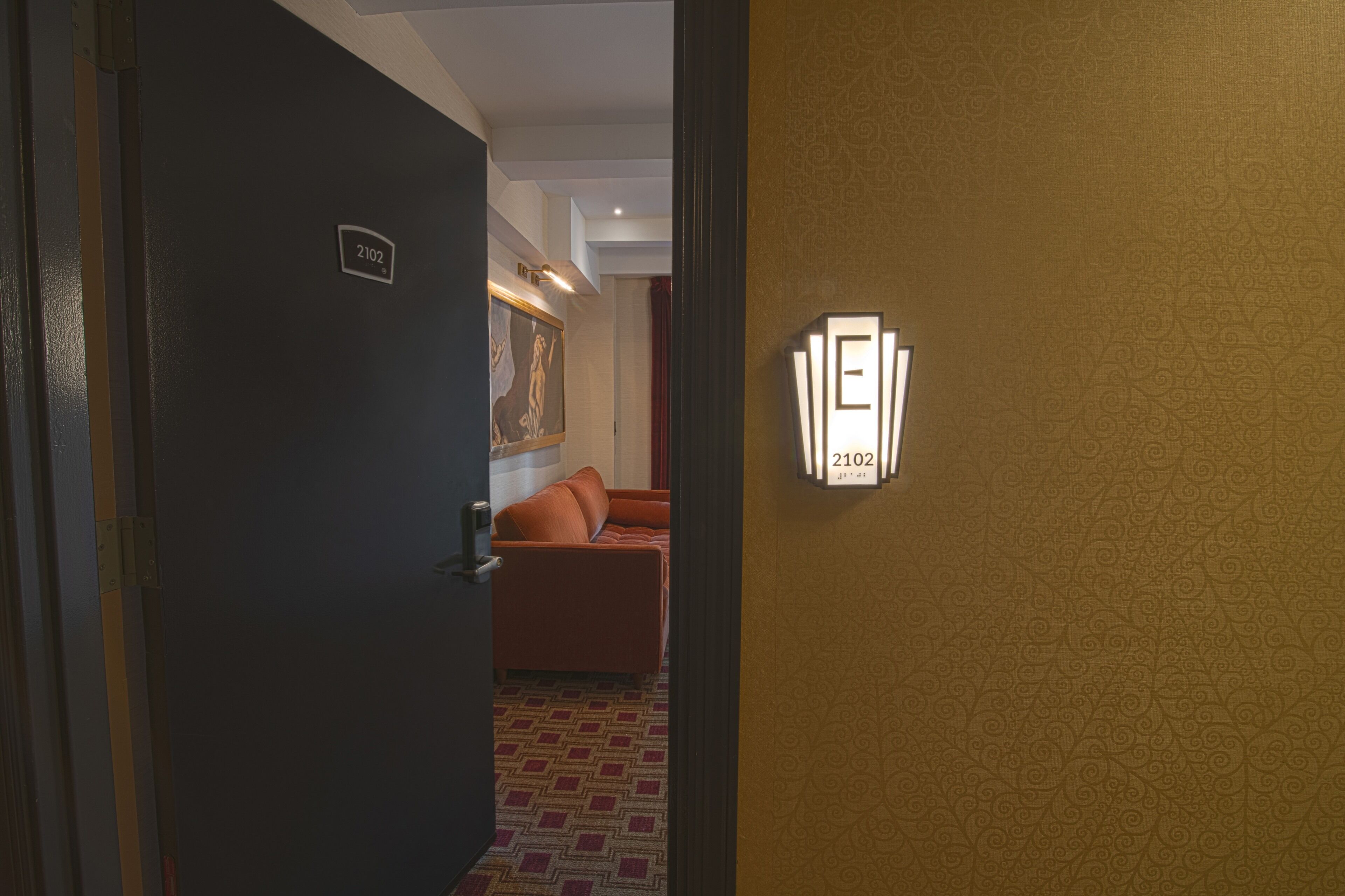 A hotel room with a door labeled '2102,' a patterned wall, and a light fixture with the number '2102' on it.