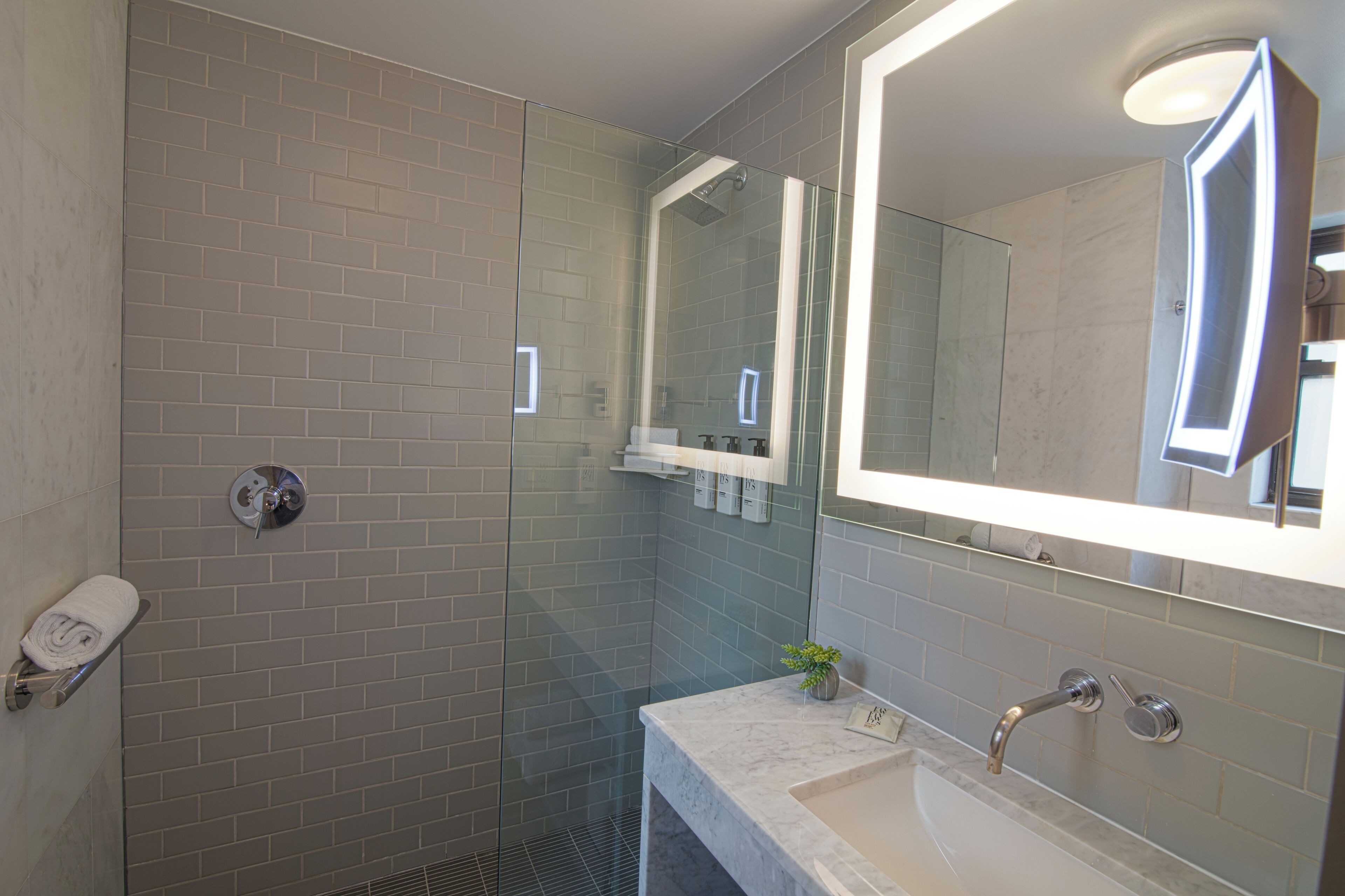 Une salle de bain moderne avec une douche à parois de verre, un lavabo en marbre et un grand miroir.