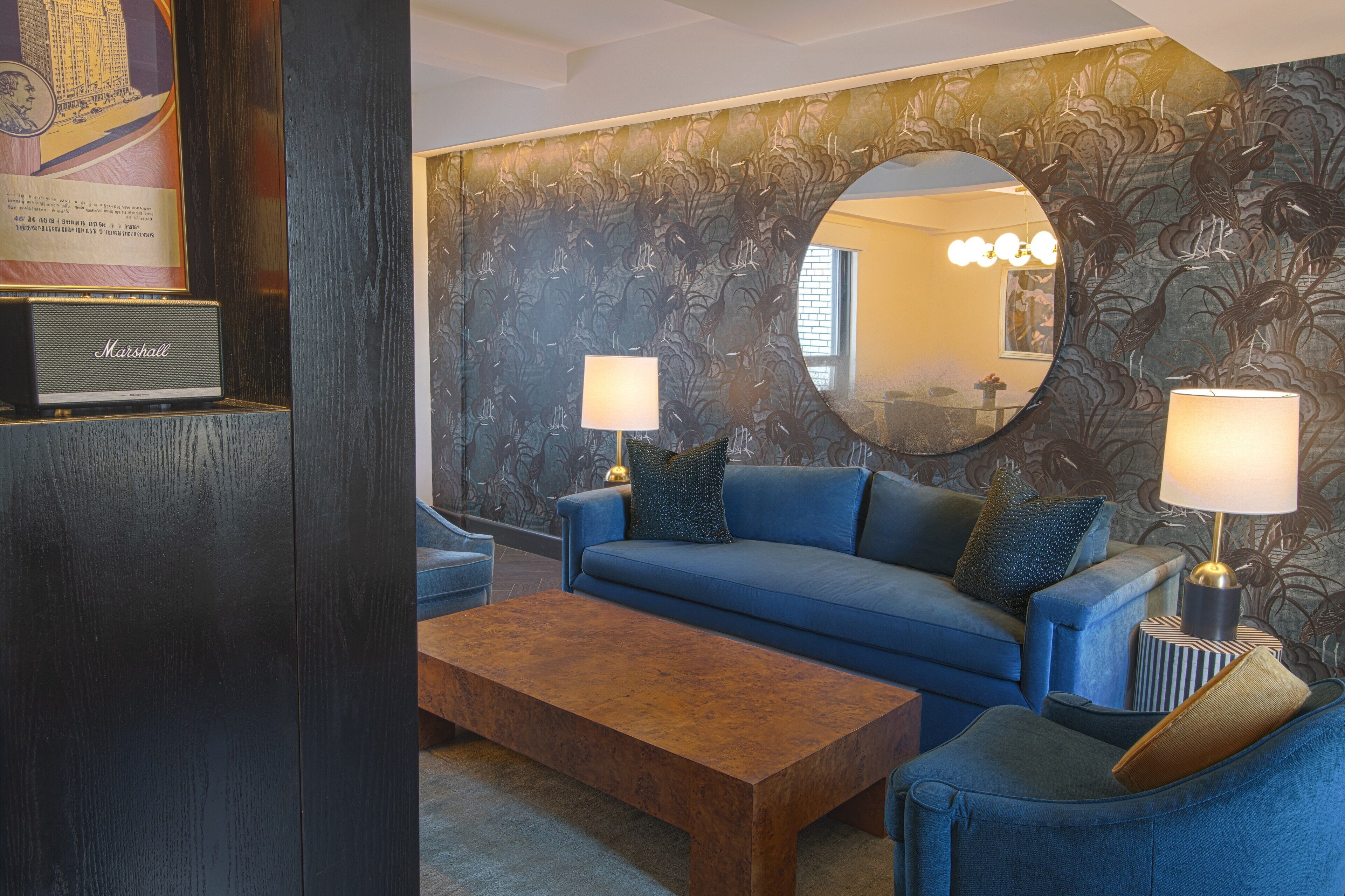 A modern living room with a blue sofa, two lamps, a coffee table, and a large mirror.