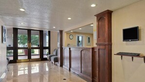 A reception area with a polished tile floor, a wooden reception desk, a clock on the wall, and a flat-screen TV mounted above a keyboard. - The Inn at Market Square (San Antonio)