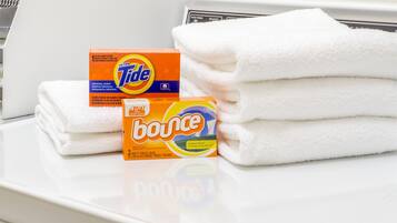 Una pila de toallas blancas y dos cajas de detergente Tide y suavizante Bounce sobre una superficie blanca.