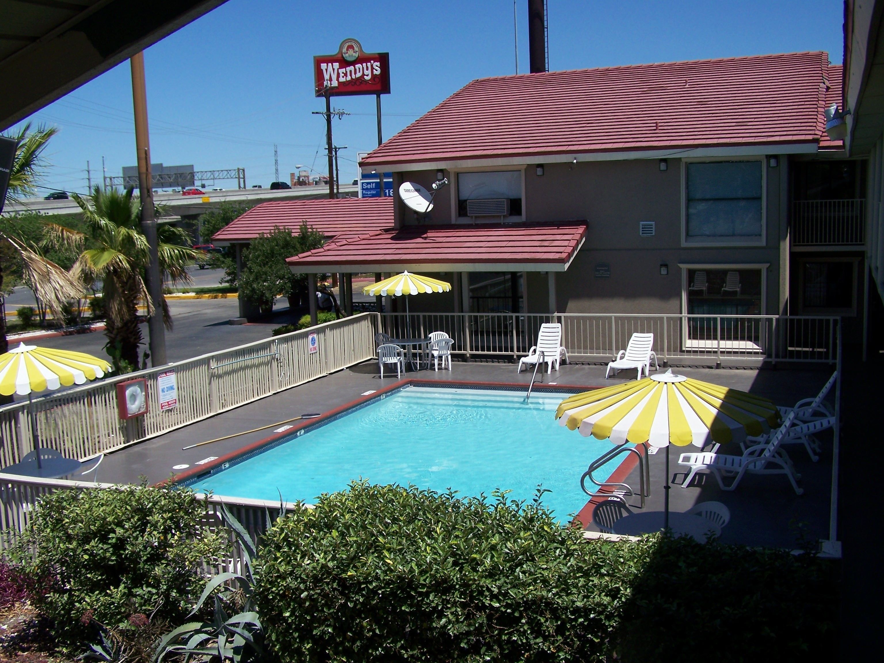 A pool area with lounge chairs and umbrellas, a Wendy's restaurant in the background, and a clear sky.