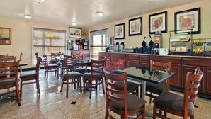 A restaurant with wooden chairs and tables, a counter with kitchen equipment, and framed artwork on the walls. - The Inn at Market Square (San Antonio)