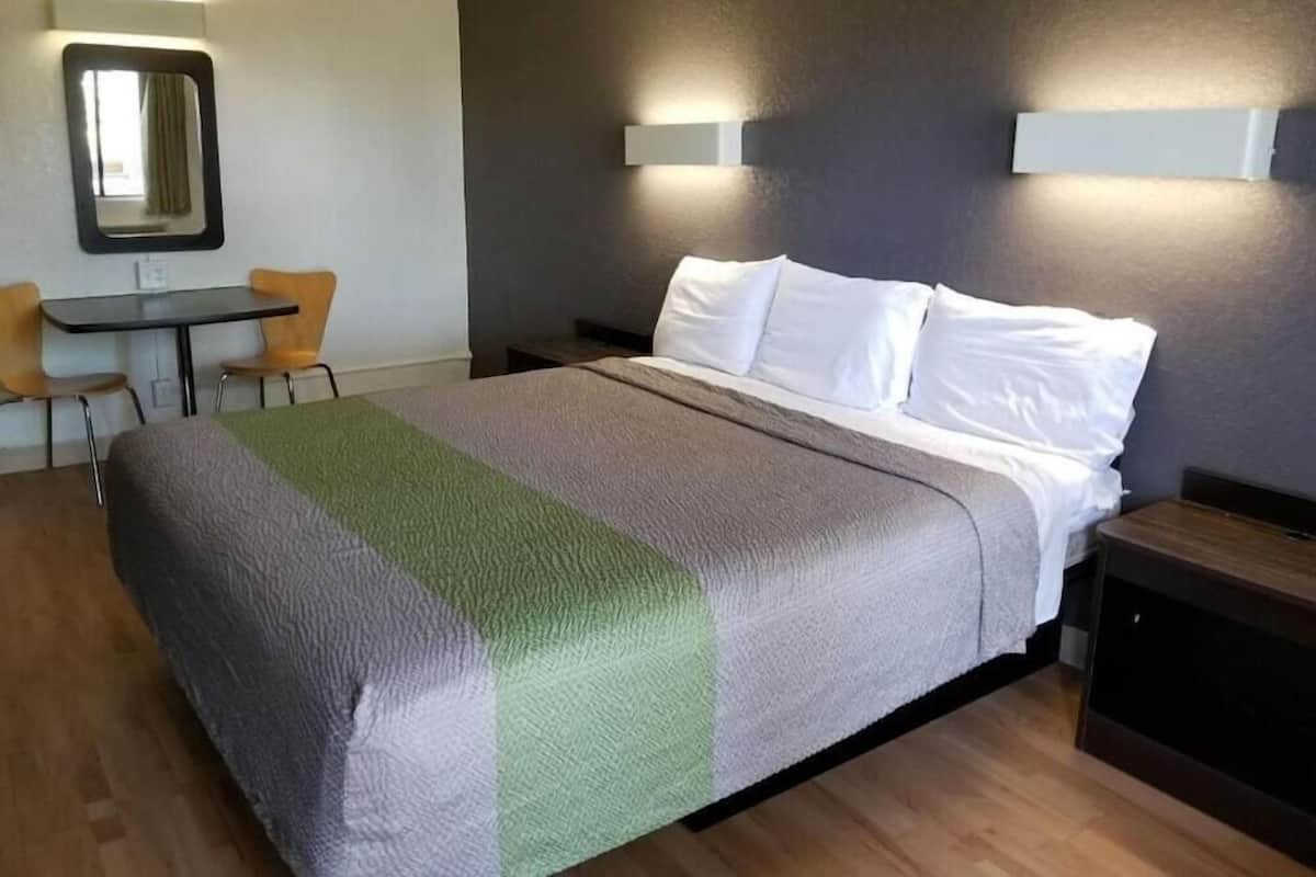 A hotel room with a bed, a small table with chairs, a mirror, and a nightstand.