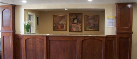 A reception area with a wooden reception desk, framed artwork on the wall, and a bulletin board.