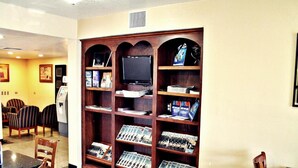 A library with wooden bookshelves, a television, and seating areas with chairs and tables. - The Inn at Market Square (San Antonio)