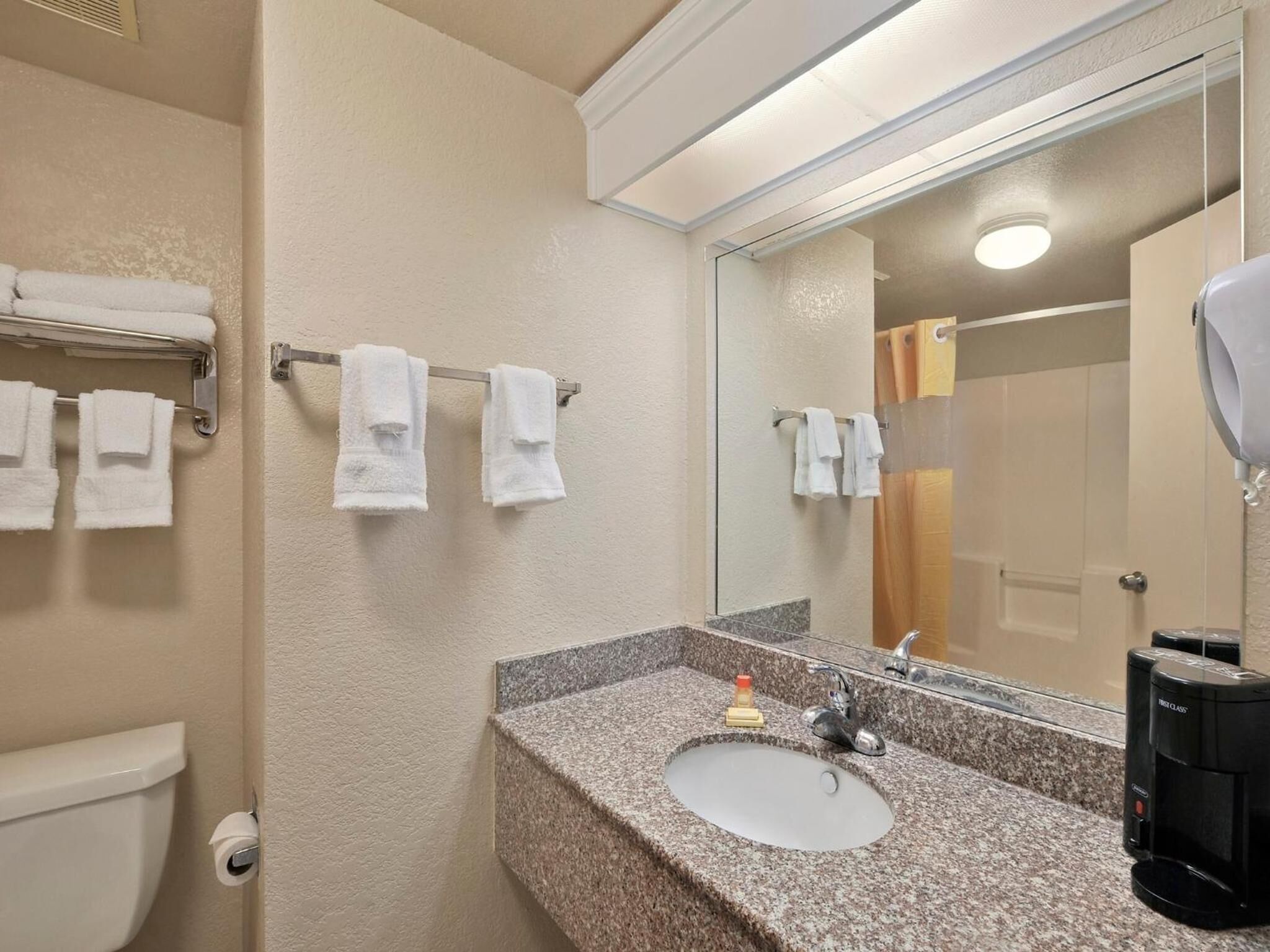 Une salle de bain avec un lavabo doté d’un plan de travail en granit, un miroir et une machine à café.