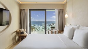 Habitación de hotel con una cama grande, un televisor montado en la pared, una mesita y vista al mar a través de puertas correderas.
