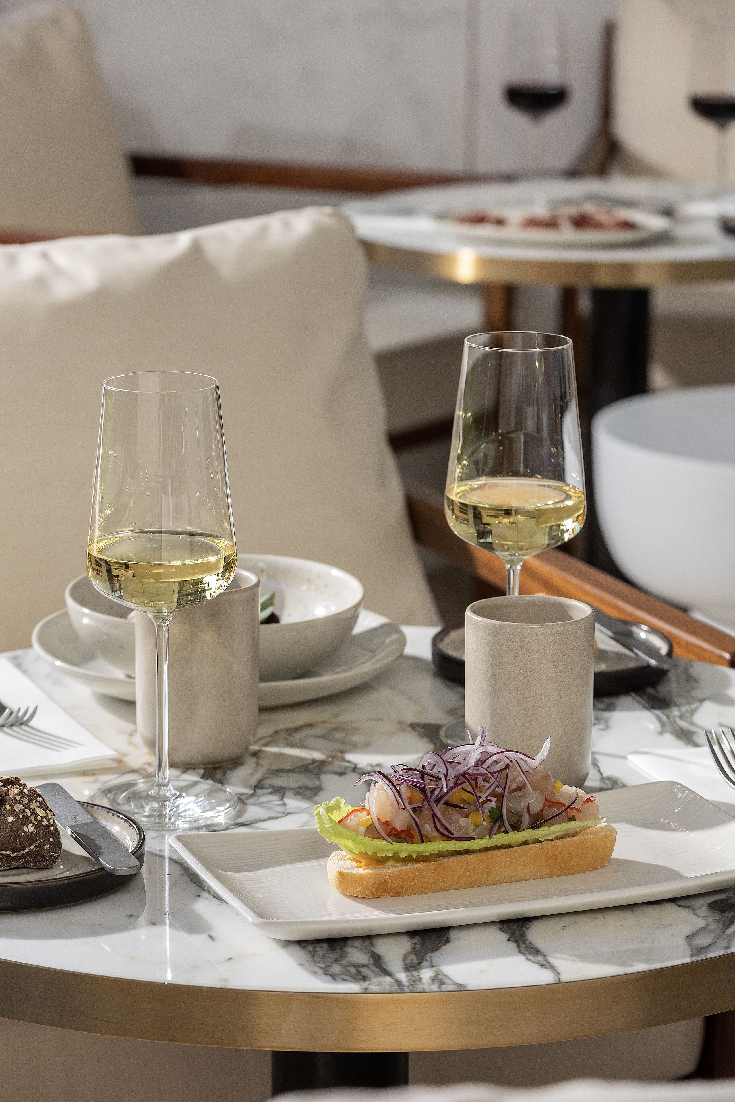 Una mesa de comedor con dos copas de vino, un plato con un sándwich y un bol de ensalada.