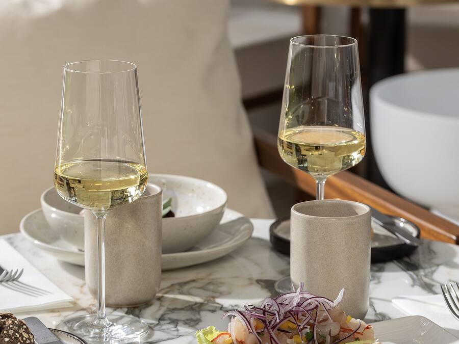 Una mesa de comedor con dos copas de vino, un plato con un sándwich y un bol de ensalada.