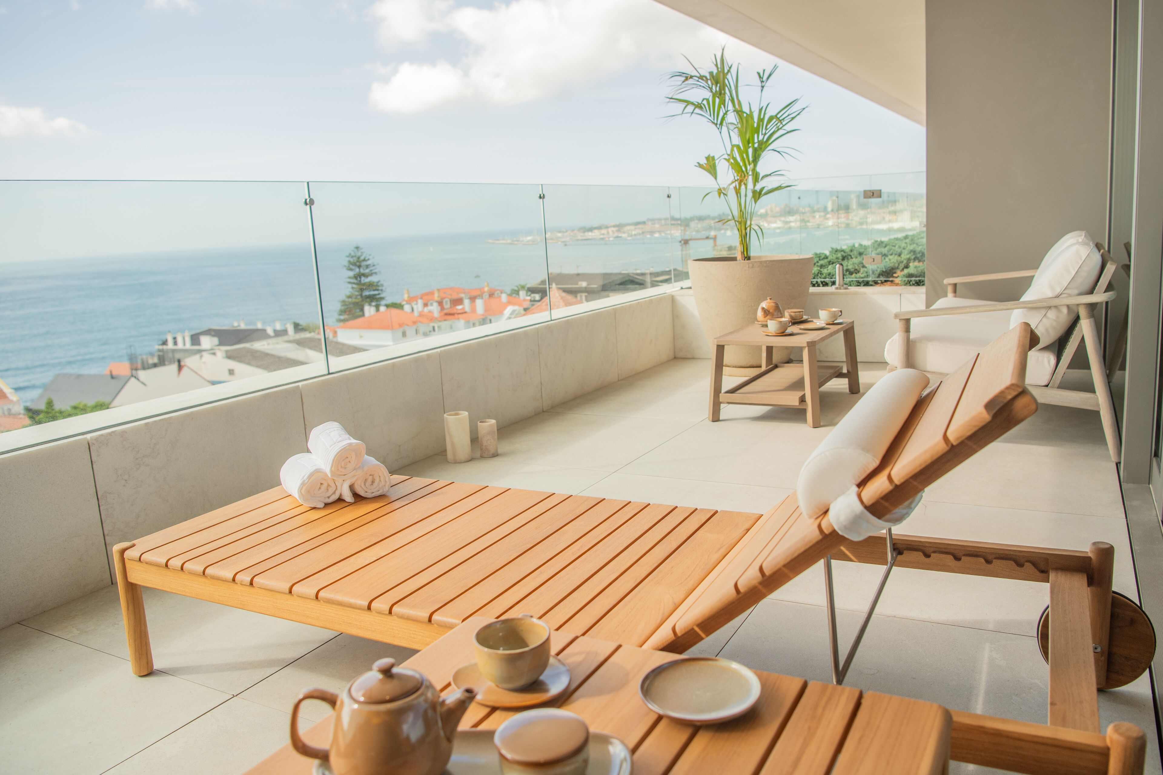 Un balcon avec une table en bois, un fauteuil de relaxation, un pot de fleurs et une vue sur la mer.