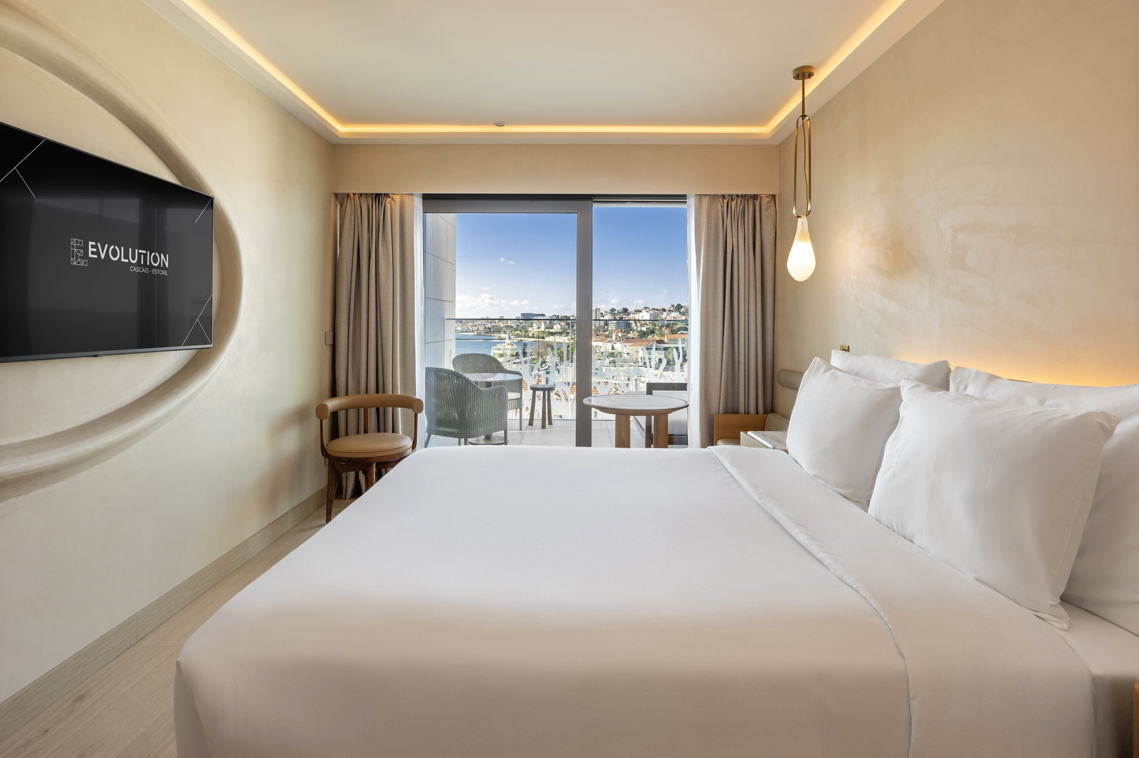 Una habitación de hotel con una cama grande, un televisor de pantalla plana en la pared, un balcón con vistas a la ciudad y una mesa con sillas.