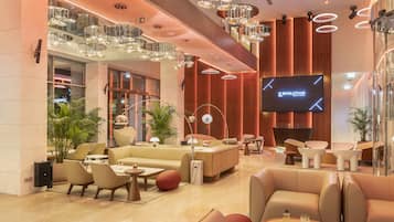 A modern hotel lobby with a large TV screen displaying 'EVOLUTION', plush seating areas, and stylish lighting fixtures.