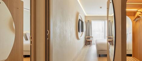 Un couloir d’hôtel moderne agrémenté de touches de bois, avec un espace salon central et un grand miroir sur le mur de droite.