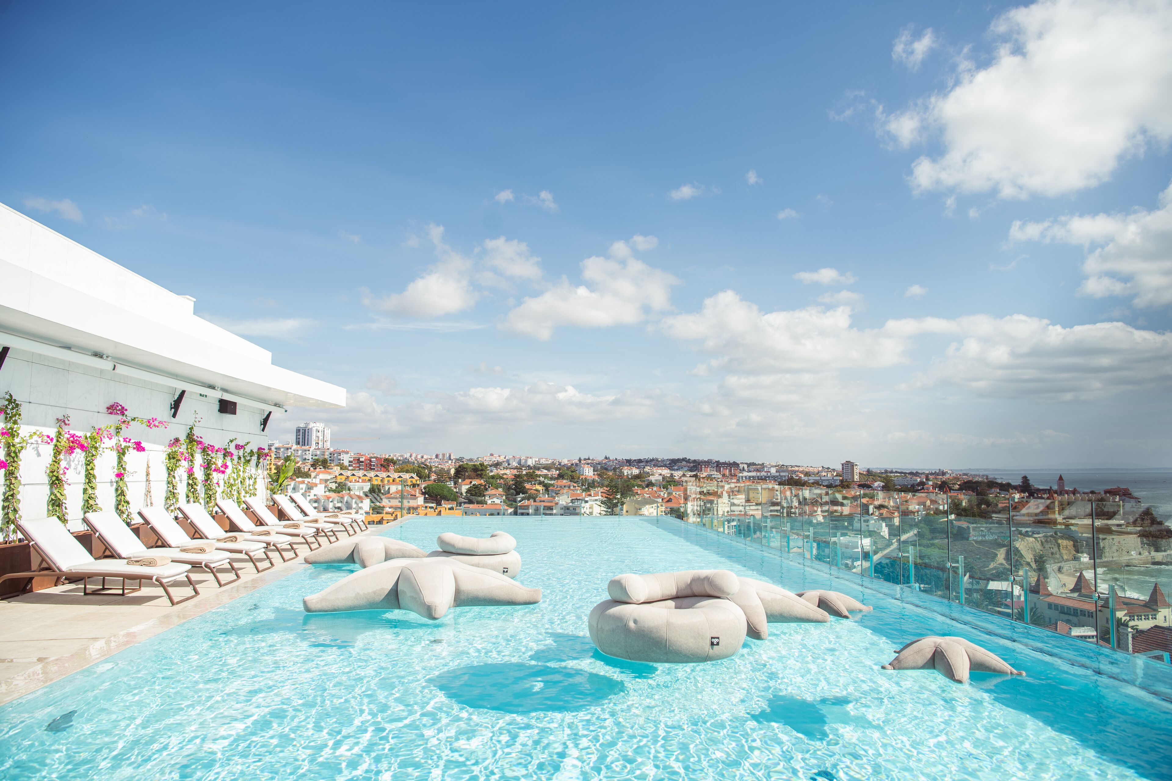 Una piscina d'hidromassatge infinit a la terrassa amb gandules i coixins decoratius, amb vista a un paisatge urbà costaner.
