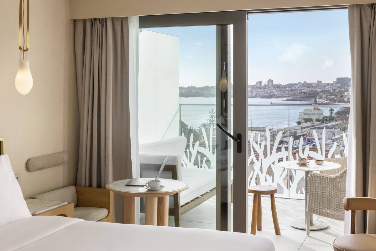 A hotel room with a balcony, a laptop on a small table, and a view of a city and water.
