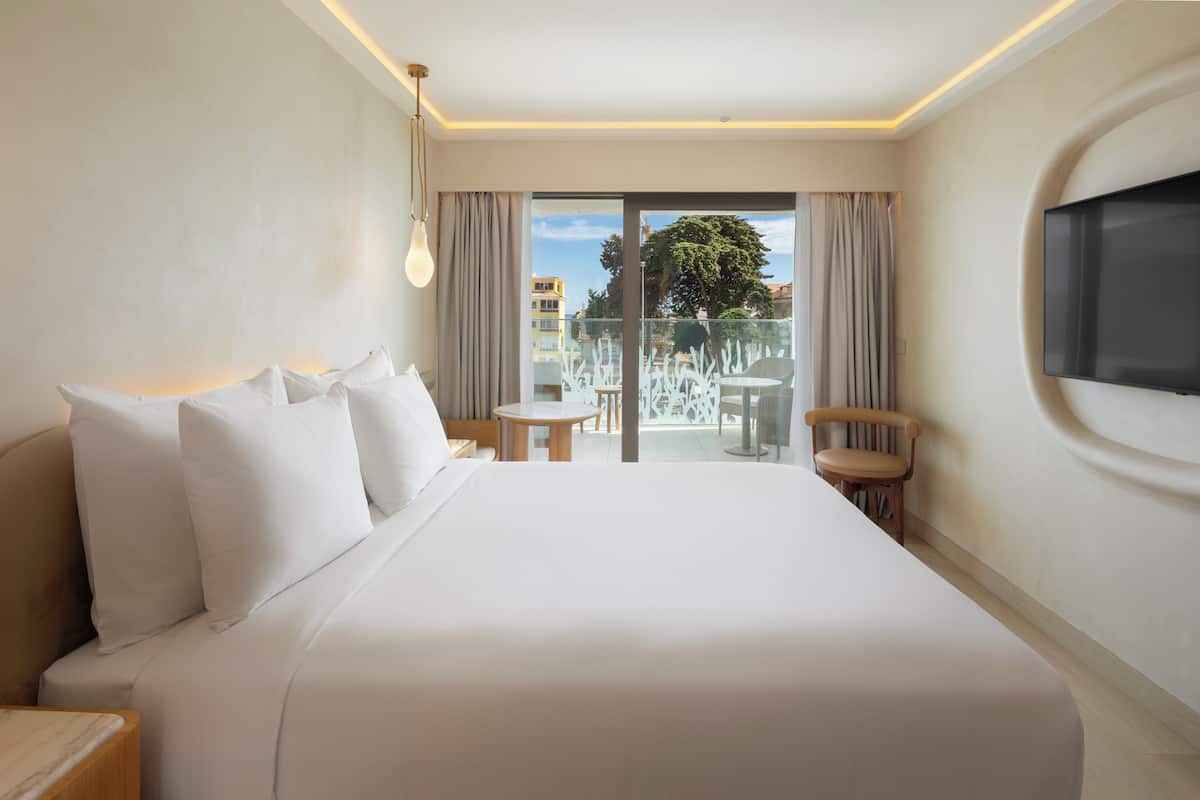 A hotel room with a large bed, a small table, a chair, and a TV mounted on the wall.
