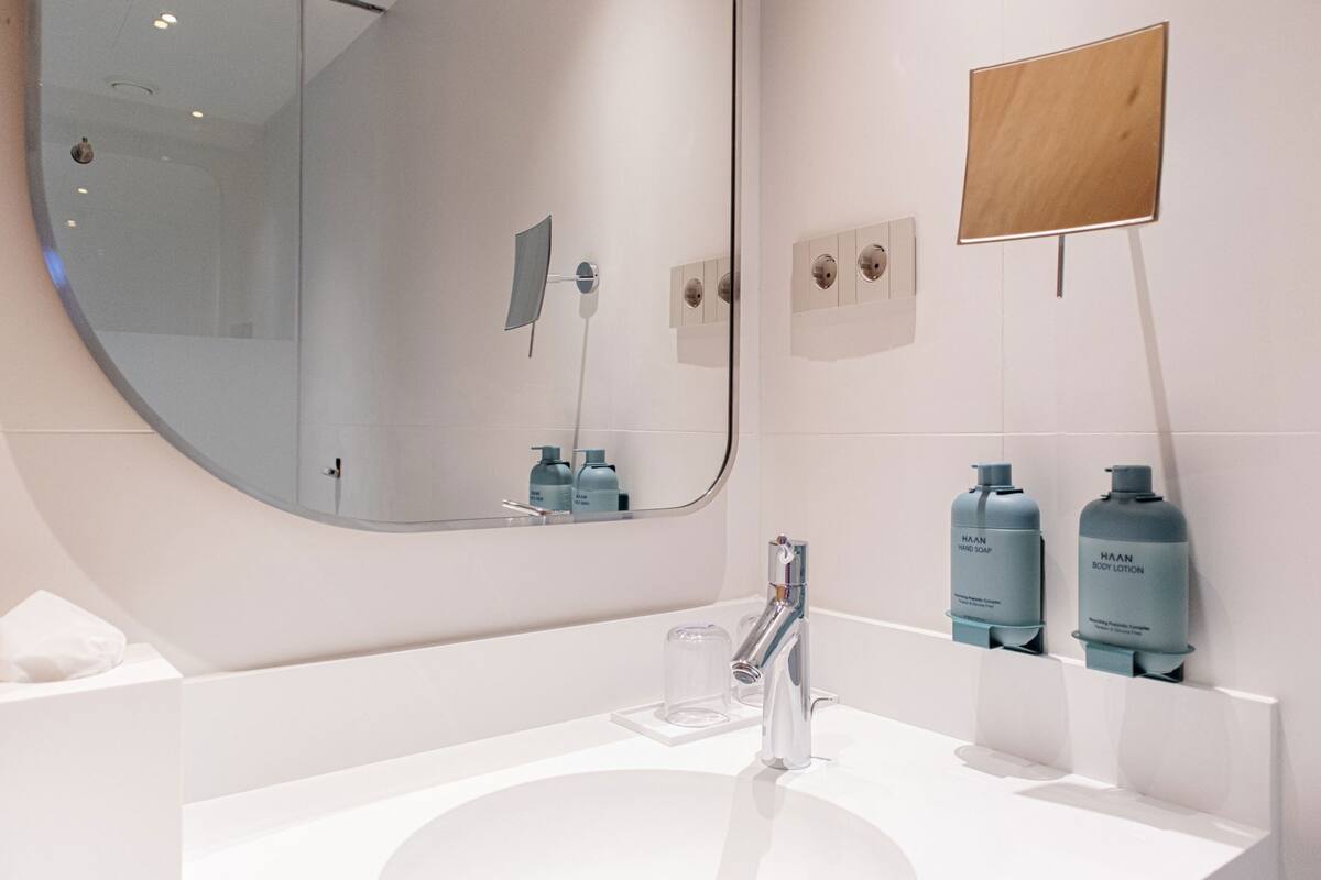 A modern bathroom with a round mirror, a white sink, and two HAAN brand bottles on the wall.