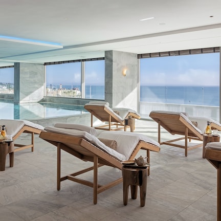 A rooftop lounge with sun loungers, a glass infinity pool, and a city view.