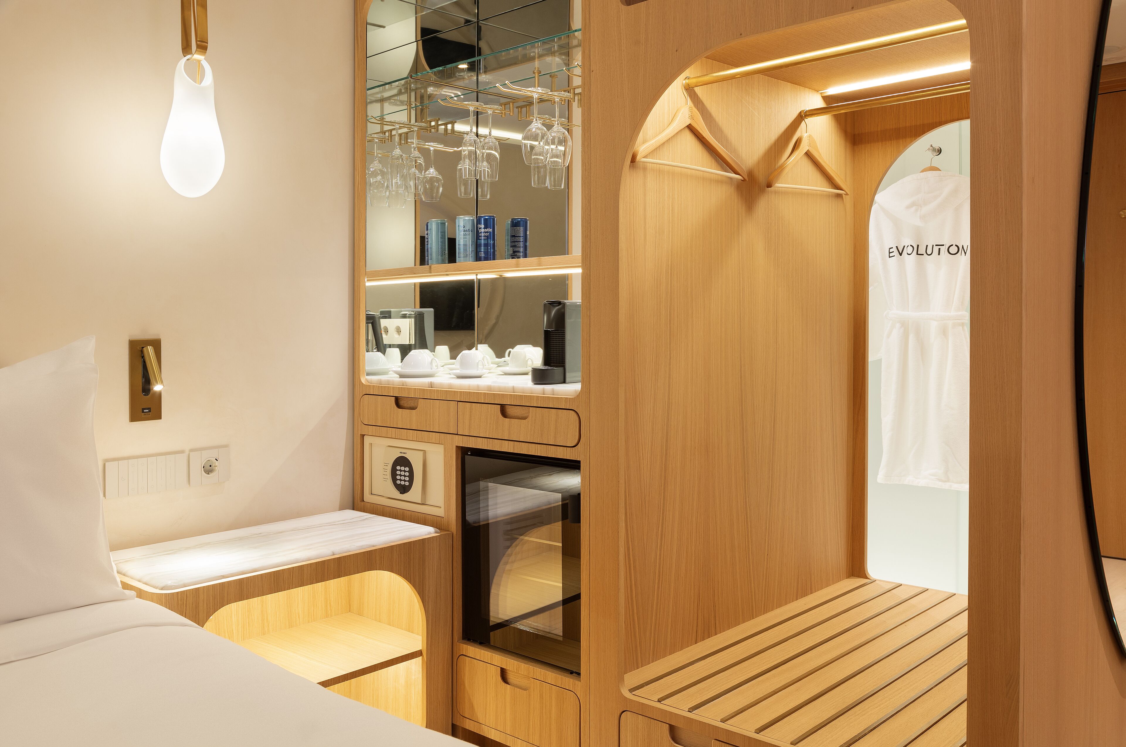 Una habitación compacta y moderna con cama, una mesita, horno empotrado y un espejo con perchero.