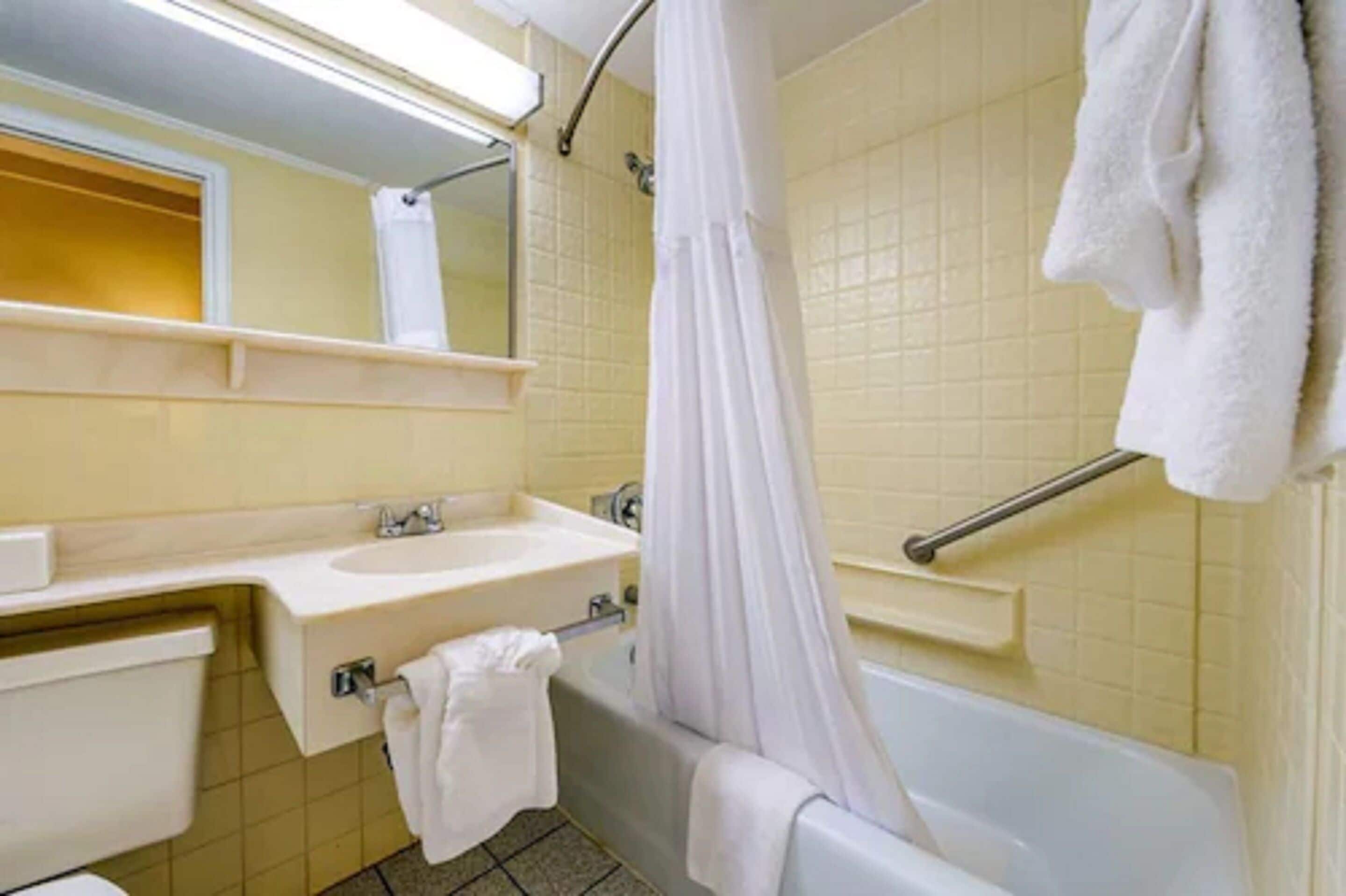 Un baño con bañera, lavamanos, espejo y barra para toallas.