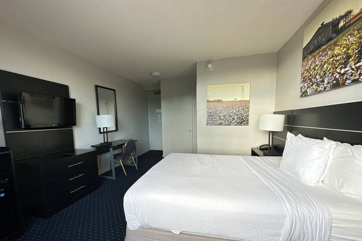 A hotel room with a large bed, a desk with a chair, a television, and a painting on the wall.