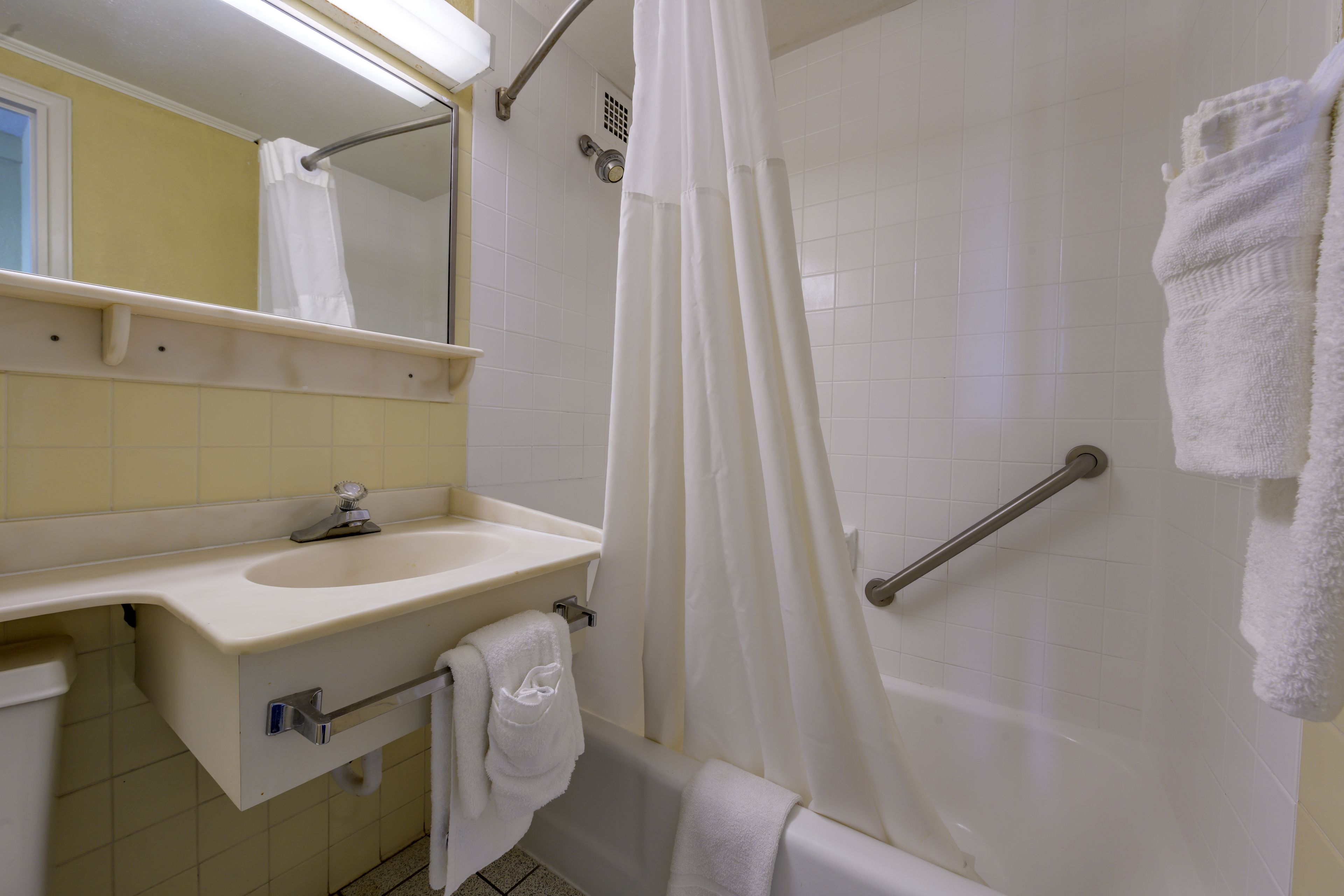 A bathroom with a sink, mirror, shower, and grab bars.