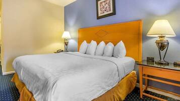 A hotel room with a large bed, two bedside tables, a wall-mounted lamp, and a framed picture on the wall.